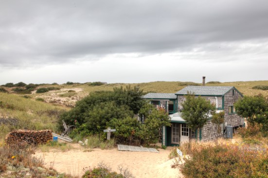 A patch of sand in front of the wood pile works as a driveway for the dune shack. The "garage" in the foreground is storage for tools, materials and dry wood. 