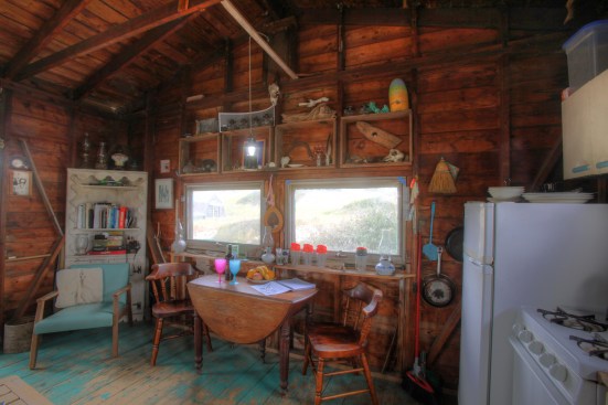 The dining area is a simple table with two chairs. Light for the table comes from a lamp on a long hook that hangs from an old oar up in the rafter ties.