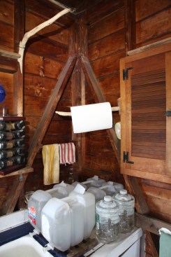 Shear strength for this part of the shack come from let-in diagonal braces at each of the corners. The upper end of the braces terminate at blocks nailed to the corner studs below the plates.This shot shows the staging for the water along with the driftwood holders for paper towels and dish towels.
