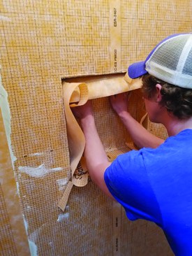 Installation. Starting at the bottom, the author aligns the back corner and presses the membrane into the back wall and bottom of the inset. He adds thinset to the bottom corners so the side flaps will adhere over the base. The side walls may then be pushed into the thinset.