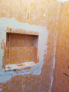 After the side walls are secure, he adds more thinset to the top of the sides to adhere the top flaps onto the walls. He then presses the flaps and ceiling of the inset in place. All that remains is to spread thinset on the surface of the shower and press the 2-inch perimeter flaps into place.