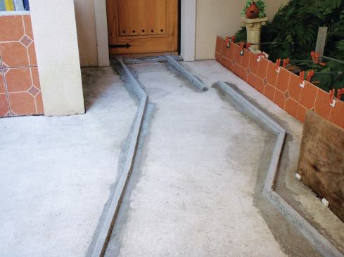 To set the slope of the mortar bed, the author created mortar screeds. The one on the left will help form a drainage swale. A third screed (not shown) runs along the left side of the path, all the way to the gate.