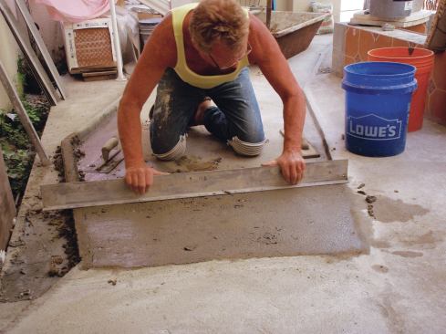 Holding the narrow face of an aluminum straightedge against the tops of the screeds, jiggle it from side to side while gradually pulling it to “saw” off or strike off the excess mortar.