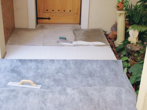 Carefully kneel on the folded sheet and using a 1/4-inch square-notched trowel held at a very low angle, comb out latex-modified thinset from the membrane fold to about 18 inches away. Flop the sheet back down, and embed it in the mortar. Pull back the sheet again, to expose bare setting bed. Repeat.