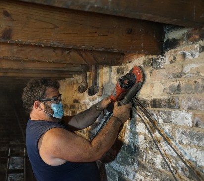 Toby Bonilla grinds down the high spots on the basement wall in preparation for installing an LVL ledger.