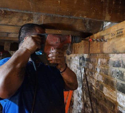 Toby drills through the ledger into the foundation wall to prep for epoxy anchors.