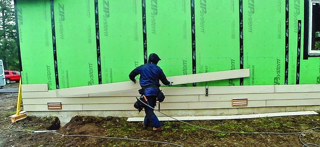 The Gecko Gauge, to the right of the author in the photo, holds a long run, making it easy for one person to install long lengths of siding.