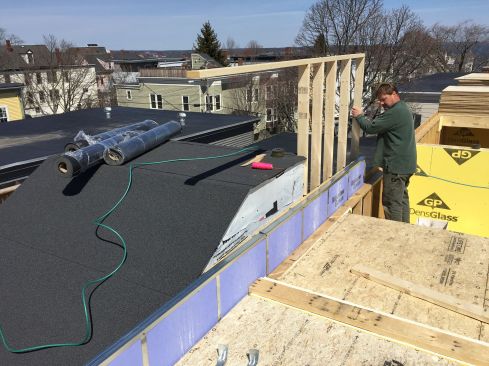 As the new building rises up above the roof of the adjacent building, the two-hour firewall rises up also. Here, Paisley works on the wall frame. The protective gypsum material must rise three feet above the top of the adjacent building's roof access structure at this location.