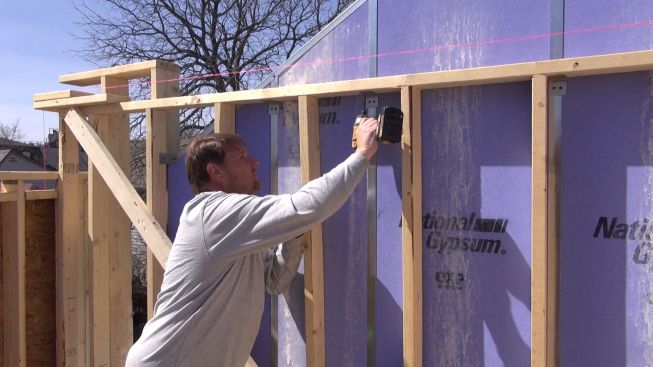 Contractor Rob Paisley fastens an aluminum breakaway clip to the wood wall frame of the new building. If the wall should catch fire, this clip would melt and allow the wall to fall away, leaving the protective gypsum board assembly intact and still fastened to the neighboring structure.