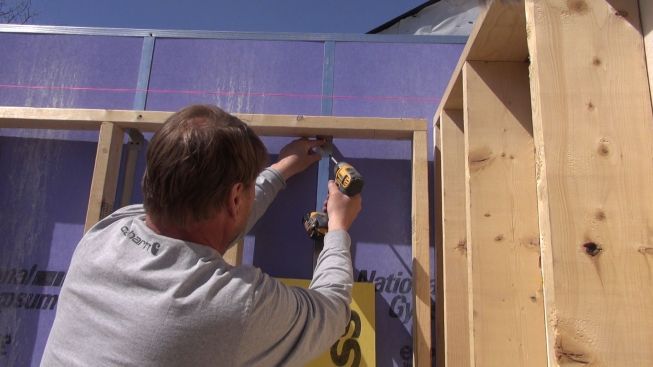 Paisley attaches the firewall frame to the wood wall of the new building with an aluminum clip.