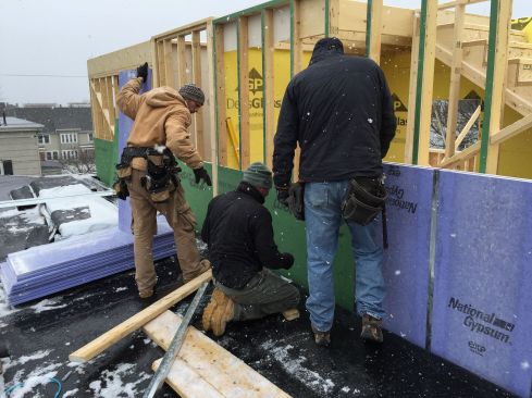 On a snowy day in spring, the crew constructs the gypsum-board and steel firewall assembly, working on the roof of the existing building next door. Later they will cover the firewall with framing and siding from this side and integrate it into the roof of the existing building.