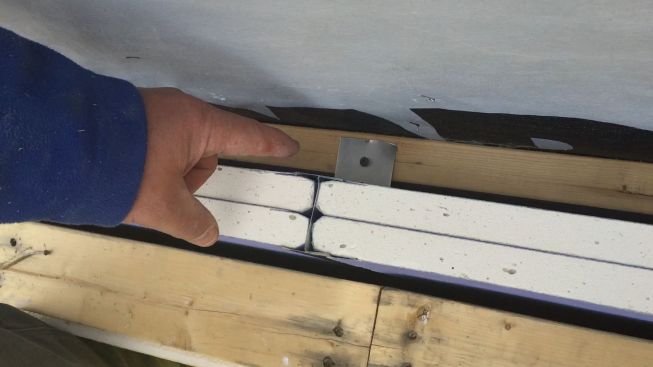 Aluminum clips hold the steel H-stud firewall framework off the wood framing, with a typical 3/4-inch gap. In a fire, the clip would melt and allow the burned framing to fall away without pulling down the wall, which would remain secured to the other building and isolate it from the fire.