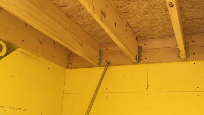 A view from underneath a stair landing within a stairwell shows the ledger for the floor frame. Structural framing is not allowed to penetrate the fire-rated gypsum board on the shaft walls, so structural screws are used to support the ledger.
