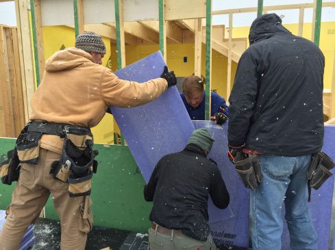 Working from the roof of the older house next door, Rob Paisley and his crew slip a two-foot by four-foot piece of National Gypsum Shaftliner eXP gypsum board into the space between their new four-story condominium building under construction.