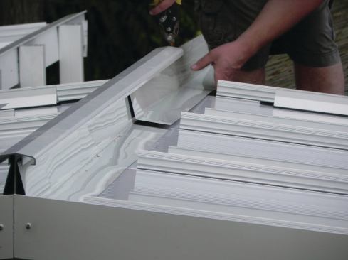 Once the panels are installed, their top edges are covered with lengths of aluminum flashing that tuck up into a downward-facing leg on the ridge beam.