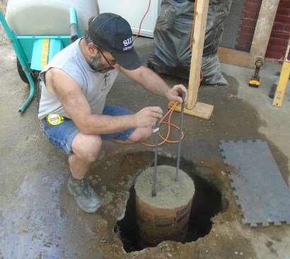 A pair of 1/2-inch rebar rods embedded in the fresh concrete will tie the pier to the expanded footing below the cardboard form, creating a more stable foundation.