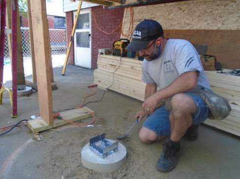 Covering the top surfaces of a galvanized post base with strips of self-adhesive membrane before setting the post in place helps to isolate the metal connector from the corrosive effects of pressure-treated lumber.