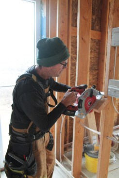 When “speed cutting,” the author aligns the left end of a scrap 2-by with the left edge of the stud on his left and registers the base of the saw against the left edge of the stud on his right, using the 1 1/2-inch offset between the saw blade and the right side of the saw base to deduct that thickness from the block he’s cutting.