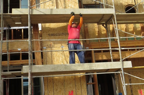 A worker for the scaffold-erection contractor sets a toe board above an access point to the building. This prevents falling objects from striking workers as they go in and out.