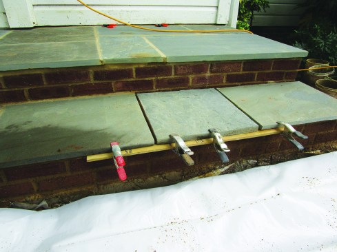 A strip of wood clamped to the pavers where they overhung the brickwork supported the grout while it cured.