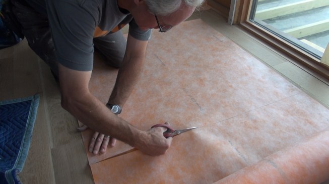 Boucher cuts a square of Kerdi membrane from a 100-foot by 1-meter roll of the material. He will apply this piece over the entire assembly of two recess boxes, then cut out for the box face openings.
