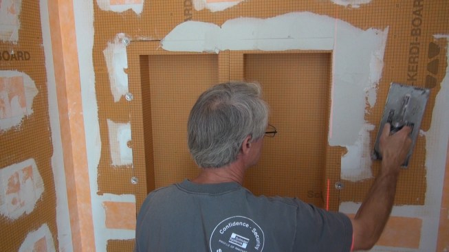 Boucher works unmodified cement mortar into the flocked face of the Kerdi-Board boxes and the surrounding wall.