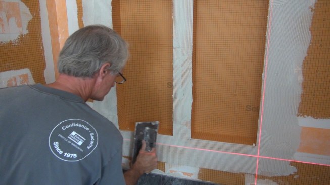 Using a Kerdi trowel with quarter-inch teeth, Boucher applies a measured amount of mortar to the wall where the membrane will be set.