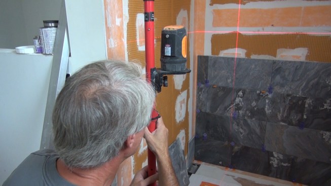 Boucher lays a laser guideline onto the wall to mark the spot for his box cut-out on the existing Kerdi-Board.