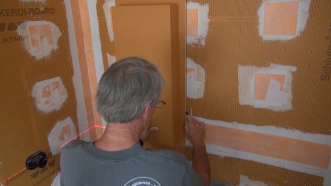 Guided by the laser layout lines, Boucher holds the pre-built recess box face to the shower wall and marks its outline for the cuts.
