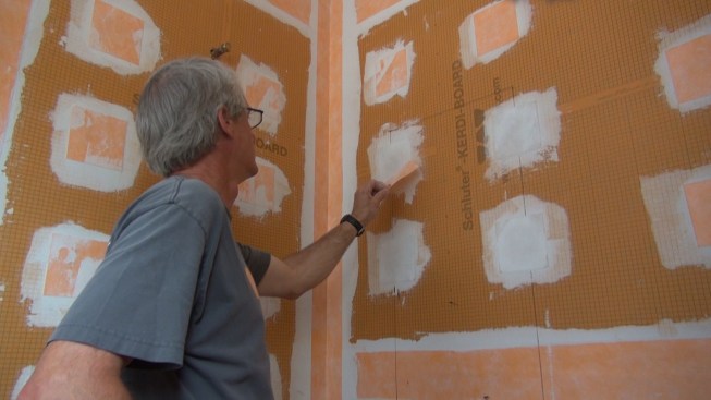 Boucher removes the previously-installed Kerdi membrane over a fastener that falls at the place where the new box must be positioned.