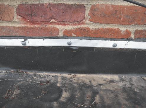 Critical-low slope details. At solid masonry walls, a termination bar (which will get lapped by a counterflashing let into the mortar joint) can work, but with brick veneer, only through-flashing will prevent leaks.