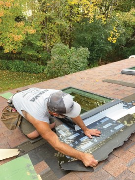 Before installing the metal head flashing, I pulled back the roofing underlayment so that I could first slide a length of 12-inch-wide Vycor underneath and lap it shingle-style over the white flexible flashing that seals the skylight to the roof deck.