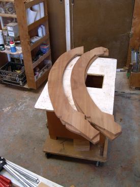 With the aid of a plywood routing template, I cut the sapele slightly oversized for the side panels for the curved braces. To guide alignment during glue-up, I added sacrificial shoulder cuts to the ends of the template; a few carefully placed brad nails held them in position for clamping. After the epoxy set, I trimmed the edges flush with the core, using a bearing-under router bit.