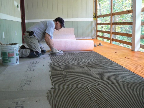 Unmodified thinset applied with a ¼-inch square-notched trowel was used to adhere the membrane to the backerboard. Working quickly, the author spread the mortar to the lines drawn to mark the position of each piece of membrane, combed it with the notched trowel, then rolled the membrane back into place.