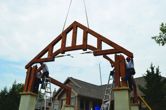 Crafted from 8x8 white-oak timbers with 8x12 plates, the 18-foot-wide frame has a 10-in-12 pitch roof. Above, a king post-and-strut truss is being lifted into position.