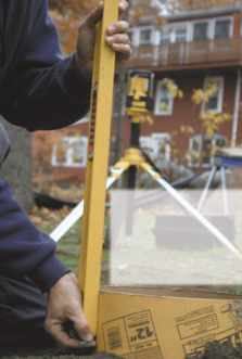 Figure 6. Using a laser level with an audible sensor, one man marks the footing forms with a nail through the cardboard, so all the concrete can be poured to the same height.