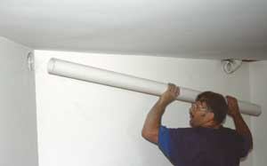 Figure 3. A length of 3-inch PVC — the lower end of which will be cemented into the slab — turns to pass through a partition wall (top). The sanitary tee will accept a second vent pipe leading to the garage. Above, the main vent line continues through a finished portion of the basement (later enclosed in a pipe chase) before exiting through an opening in the band joist. Like plumbing vent pipe, radon venting must be pitched enough to allow condensate and rainwater to drain.