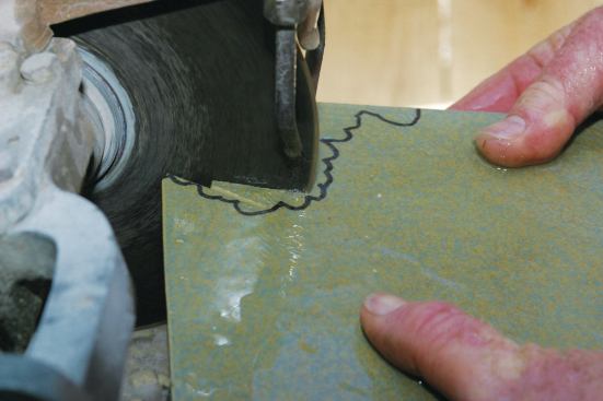IRREGULAR CURVED CUTS

I make any irregular tile cuts freehand. The first step is to make a series of straight cuts toward the mark (11, 12). Next, I make additional shorter cuts, gradually getting closer to the mark (13). Finally, when the cuts are about 1/8 inch away from the mark, I use the side of the blade to finish the cut (14). With all freehand cuts, I keep the plane of the tile aimed at the arbor so that the shoulder of the cut is square to the surface of the tile. If held lower, the cut edge tapers out, and the tile probably won’t fit where it’s supposed to go (15).

Keep in mind that the wet saw in these freehand cutting photos is over 65 years old and cannot straight cut tiles larger than 6 inches. Although it is not suitable for working with today’s larger-size tiles, I still use it a lot for intricate freehand cutting. You can cut just about any shape you want with a wet saw simply by following the steps outlined above.

I should point out that freehand cutting causes irregular blade wear, and once a blade is used for this technique, it should not be used to make straight cuts. Generally, I use a blade for straight cutting until roughly a third of its cutting rim remains. I then use the remainder of the blade for freehand work. When the blade is no longer effective for freehand cutting, I still don’t toss it; I extend its life by using what’s left of the diamond rim to sharpen carbide-tipped drill bits.