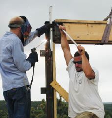 Because steel parts tend to pull toward the bead during welding, a worker uses an extension handle on the rigger’s wrench to steady a beam while the welder applies a tack.