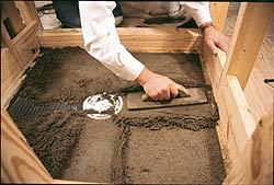A bed of latex-modified mortar is troweled into the wire lath, using the float strips and the drain flange to gauge the slope.