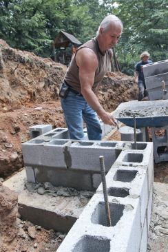 A mason fills the rebar-containing cells in the concrete-block retaining wall with grout.