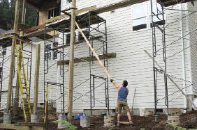 Lifting the posts took strength and planning. Two 2x4s screwed to the post with 5-inch LedgerLoks (FastenMaster; 800/518-3569, fastenmaster.com) served as handles (top). Once the post was high enough to rest on a 2x4, the author changed position (middle). Catches made of framing lumber secured the raised posts to scaffold (bottom).