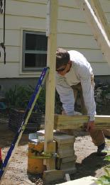 Before raising the post, the base of the 2x4 “assistant” is attached to the post’s concrete pier with a nylon load strap and secured plumb with the braces.