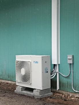 Refrigerant lines and wiring on the exterior wall are protected with a vinyl or sheet-metal cover. Condensate drain tubes are visible at lower right.