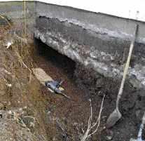 After digging a trench alongside the existing front-wall footing with an excavator, the author's crew used hand tools and a rotary hammer fitted with a chisel to remove the compacted soil under the footing.