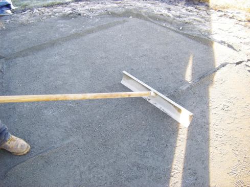 Before laying pavers, the crew removes the screed guides and fills the resulting troughs in the bedding layer with sand.