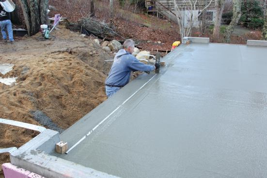 To create a weather lip at the garage doors, the foundation contractor sinks a length of galvanized pipe into the wet concrete, then finishes the sloping apron in front.