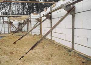 The author's site-made staging brackets provide lateral support to the ICF wall forms during the pour, as well as access to the top of the forms for pumping concrete and setting the anchor bolts and sill plate. Backers on the opposite side of the wall provide external bracing and catch the 16-inch-long screws used to attach the staging to the form work.