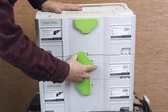 The top handle recesses into the lid so another box can be stacked on top of it; the two boxes are joined at the rear by mating slots and tabs and at the front by a rotating T-Loc mechanism.