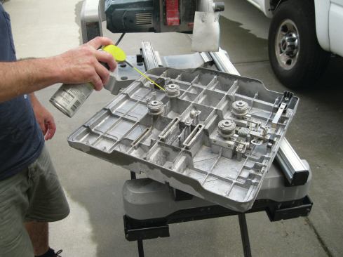 Four sealed bearings on the bottom of the sliding table guide it along the rails. The tile setter has removed the table to clean off the sludge and is spraying silicone lubricant onto the bearings.
